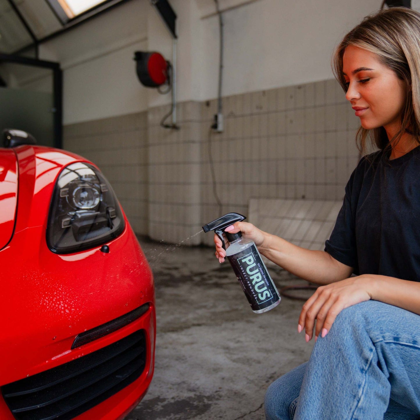 Vrouw gebruikt PURUS Insect Remover spray op rode auto voor veilig verwijderen van insectenresten op carrosserie en ruit