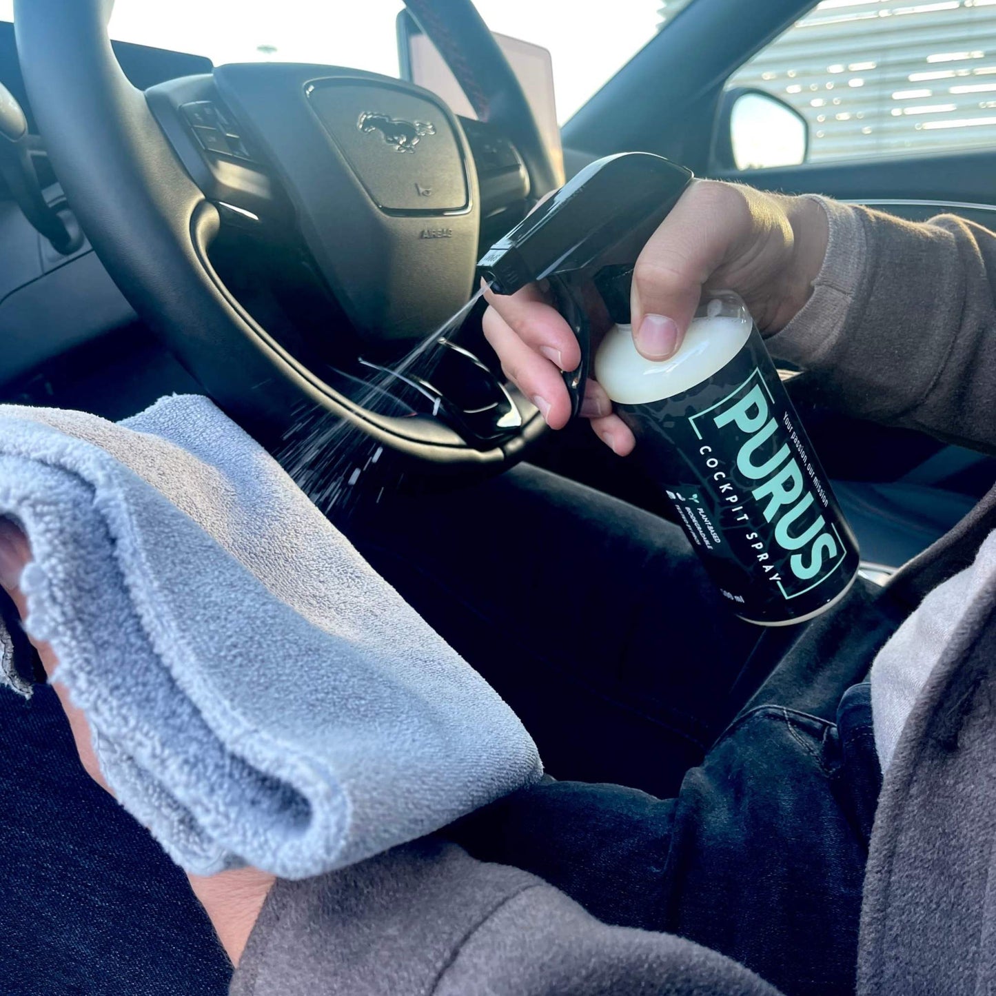 Person die PURUS Cockpit Spray spuit op microvezeldoek voor interieurreiniging van auto met Interior Kit - Leather
