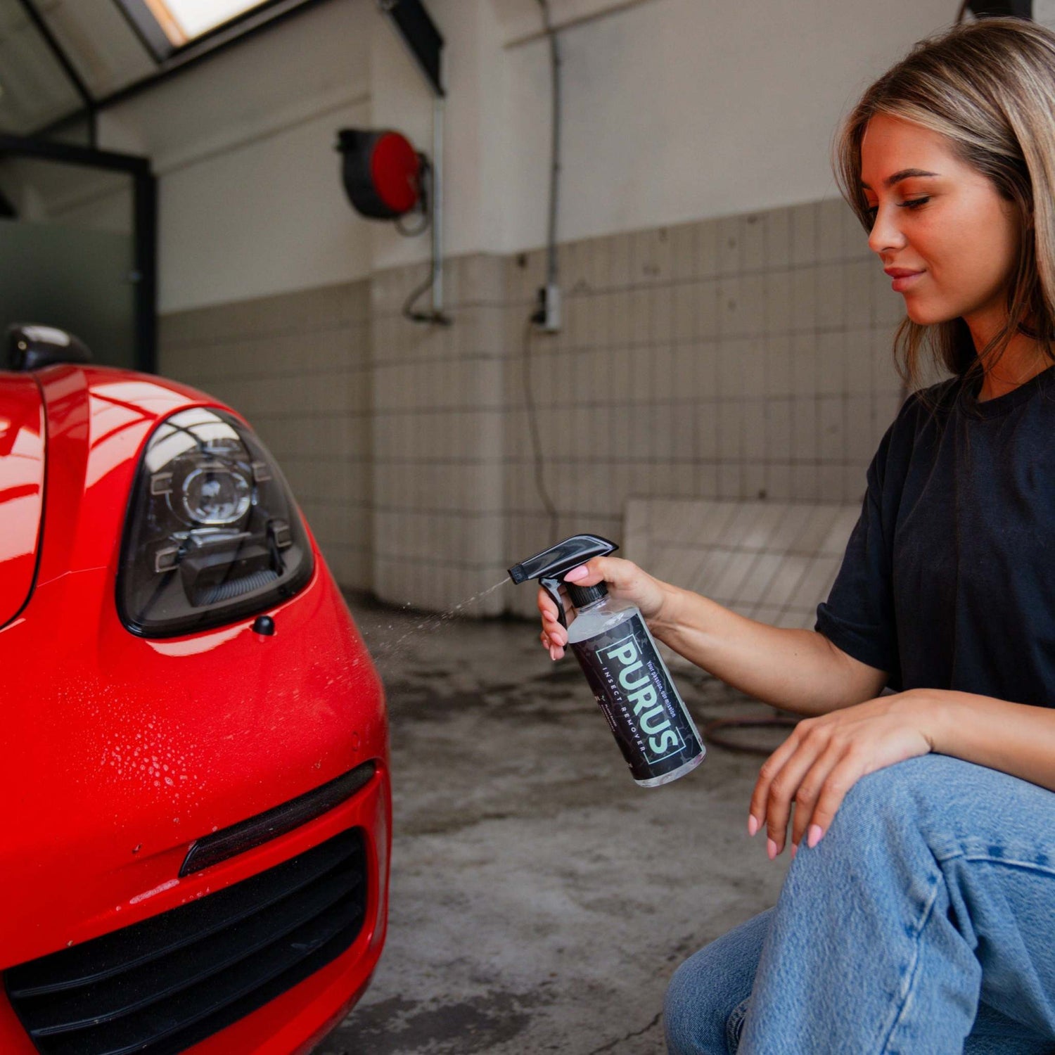 Vrouw gebruikt PURUS Insect Remover spray op rode auto voor veilig verwijderen van insectenresten op carrosserie en ruit